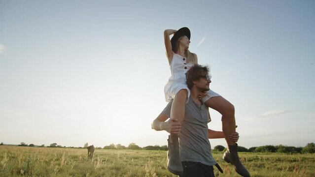 Enamored man carrying girlfriend on shoulders on meadow in countryside