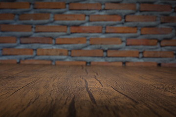 A wooden table surface in a dark room with a centered illuminated area for placing items against a blurred brick wall backdrop.