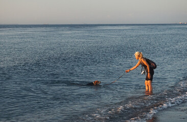 A Woman playing at the beach with the dogs.