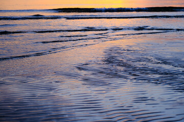 Beautiful sunset view on the beach. Colorful sea beach sunset with golden light reflected on the water surface and soft waves. Summer vacation and travel concept.