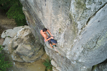 Determined climber clambering up steep wall of rocky mountain. Sportsman overcoming difficult route. Engaging in extreme sports and rock climbing hobby concept