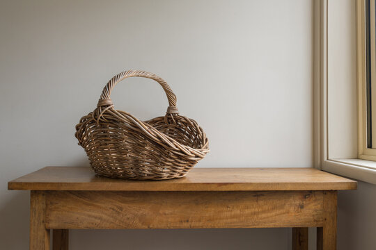 Empty wicker basket on oak sidetable against beige wall next to window (selective focus)