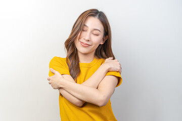 Smiling positive, hugging oneself happy asian young woman wearing yellow casual, portrait of beautiful brunette with long hair, self love and self care, expression hug standing isolated on background.