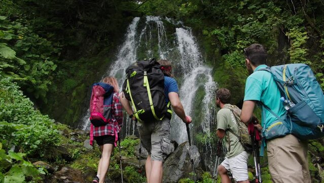 Team building, rest with colleagues in mountains. Group of tourists watching water fall from cliff