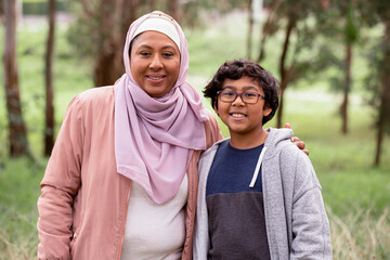 Smiling middle aged woman wearing pink hijab and smiling boy with curly hair wearing eye glasses