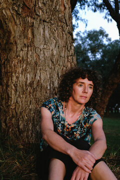 Woman sitting against trunk of tree in golden light
