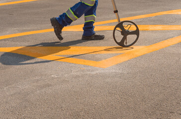 Measuring the freshly painted yellow strips. Worker and traffic sign.