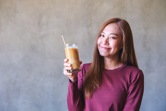 Portrait image of a young woman holding and drinking iced coffee
