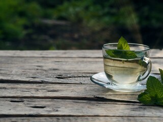 Medicinal herbal tea in a glass cup with mint leaves on a natural background.