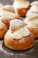 Obraz na płótnie Canvas Traditional winter sweet: Semla semlor or fastlagsbulle flavored with cardamom, filled with almond paste and whipped cream closeup on the table. Vertical