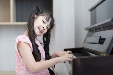 Happy child girl playing the piano at the school. Smiling girl practice play piano in living room at home. Education and skill concept.