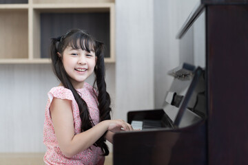 Fototapeta na wymiar Happy child girl playing the piano at the school. Smiling girl practice play piano in living room at home. Education and skill concept.