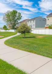 Vertical Whispy white clouds Concrete pathway in the middle of a green field with trees in a residential area at Utah valley
