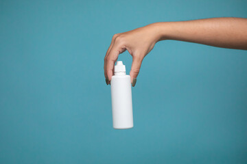 A bottle of liquid for lenses in woman hand on a blue background. Mock up of liquid for lenses