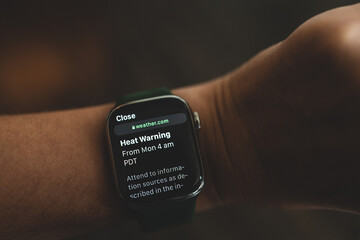 Woman is looking at the smart watch with message Heat Warning on display