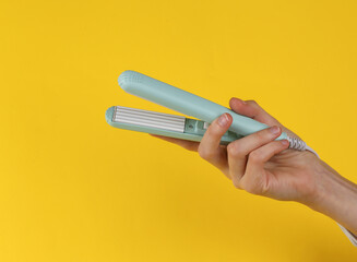 Mini Hair straightener in female hand on a yellow background.