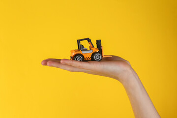 Mini model yellow taxi car in female hand on yellow background.