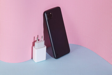 Smartphone with charging adapter on a blue-pink background. Creative layout, minimal still life, modern gadgets
