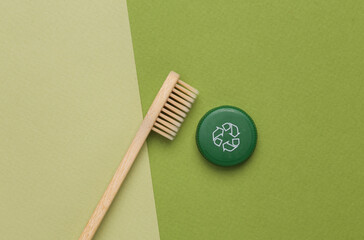 Plastic bottle cap with circular recycling symbol and eco wooden toothbrush on green background. Round recycle concept