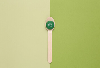 Plastic bottle cap with circular recycling symbol and eco wooden spoon on green background. Round recycle concept