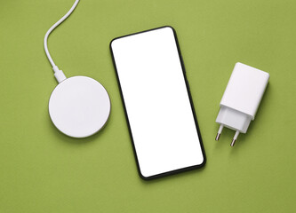 Smartphone with white blank screen, wireless charging platform and classic charging adapter on...