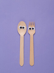 Wooden fork and spoon with eyes on purple background. Creative layout