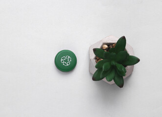 Plastic bottle cap with circular recycling symbol and plant on gray background. Round recycle concept