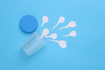 Sperm analysis, spermogram. A jar for analysis with paper-cut sperm on blue background. Man's health