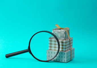 Stack of Christmas gift boxes wrapped in a bow with magnifying glass on turquoise background