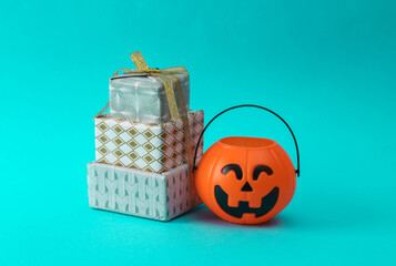 Stack of Christmas gift boxes wrapped in bow with a Halloween bucket on turquoise background