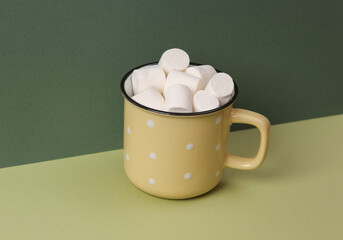 Cup with marshmallows on a green two-tone background. Minimal still life