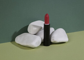 Aesthetic beauty or fashion still life. Red Lipstick tube with stone on two tone green background. Makeup concept, Natural cosmetics