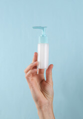 Cream bottle in female hand on a blue background.