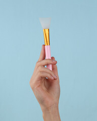 Makeup plastick brush in female hand on a blue background.