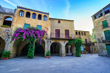 Square of the picturesque medieval village of Peratallada with arches and flowers on the walls of the houses, Girona, Spain.