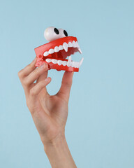 Jumping clockwork joke jaw with fangs in female hand on blue background.
