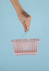 Mini supermarket basket in female hand on a blue background.