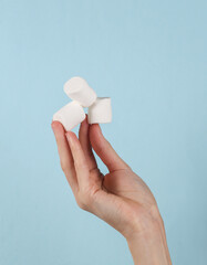 Marshmallows in female hand on a blue background