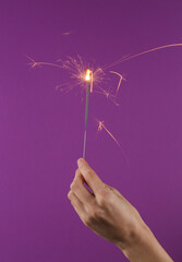 Sparkling bengal fire in female hand on purple background