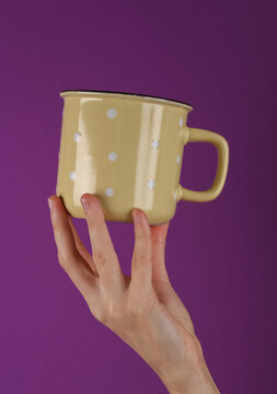 Ceramic yellow cup in female hand on purple background