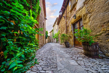 Picturesque alley with stone houses and cobblestone floor, plants and vines at golden sunset, Peratallada, Girona, Catalonia.