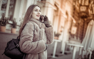 Young attractive fashion blonde woman dressed in fur coat talking on the phone in city