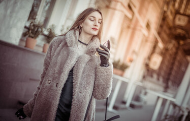 Attractive fashion woman in a fur coat holding bottle of luxury perfume in the city
