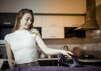 Cheerful caucasian woman ironing things with an iron on ironing board in a living room