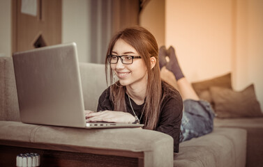 Young business woman looks into the laptop screen while sitting on the sofa in the living room. Online education or work from home