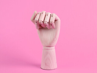 Wooden hand shows a fist gesture on pink background. Feminism symbol