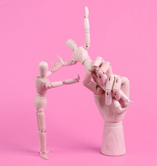 Wooden Hand holds a puppet on pink background. Control