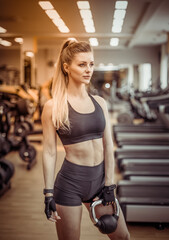 Fototapeta na wymiar Sexy young fit woman with a perfect body dressed in sportswear trains with a kettlebell in a modern gym. Healthy lifestyle