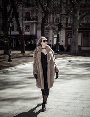 Fototapeta premium Fashion woman in warm fur coat, gloves and sunglasses walking in city