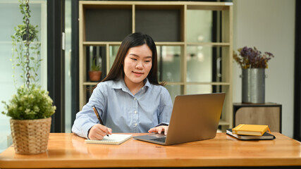 Beautiful female employee using laptop computer at bright modern corporate office